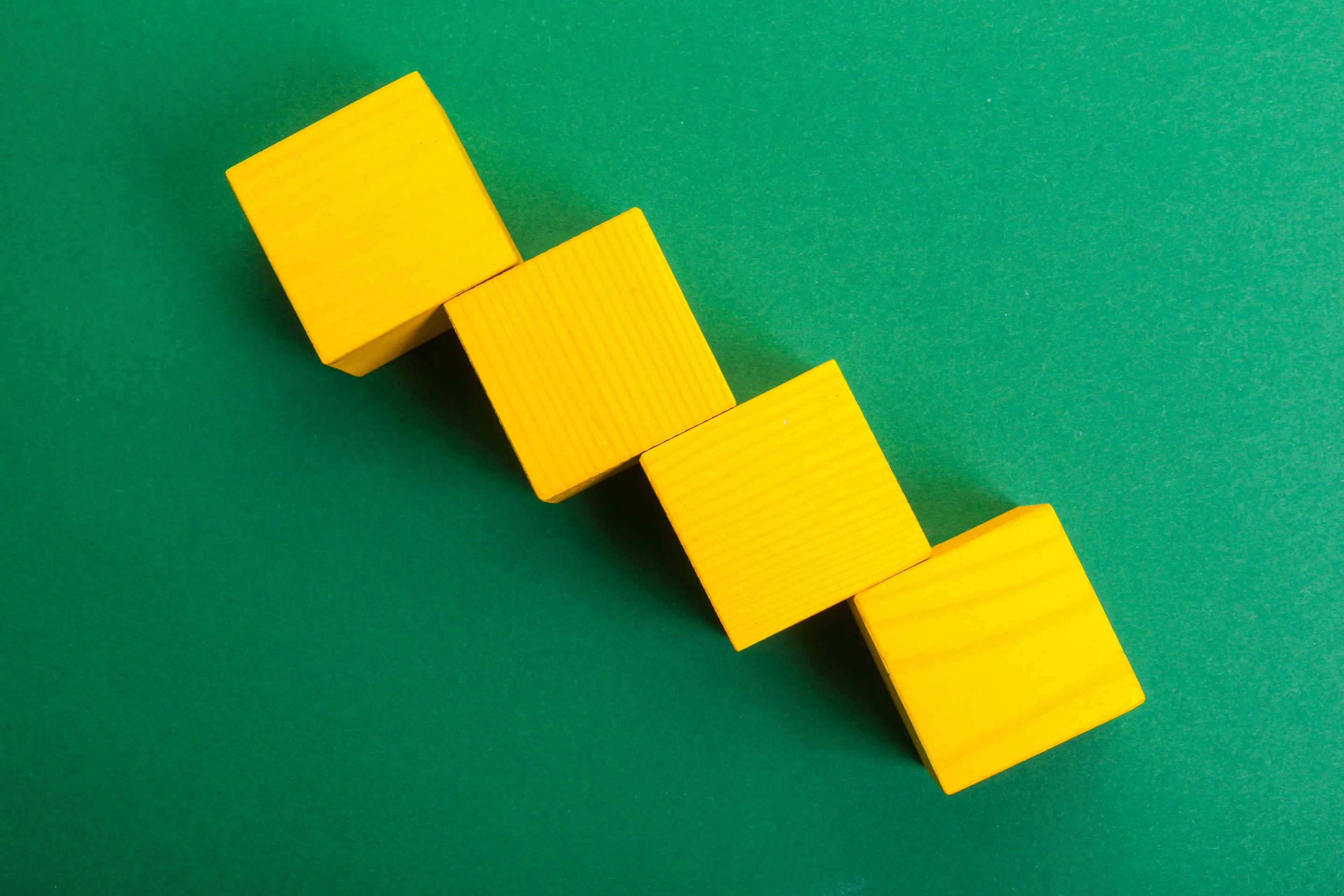 Four yellow wooden blocks stacked diagonally on a green background